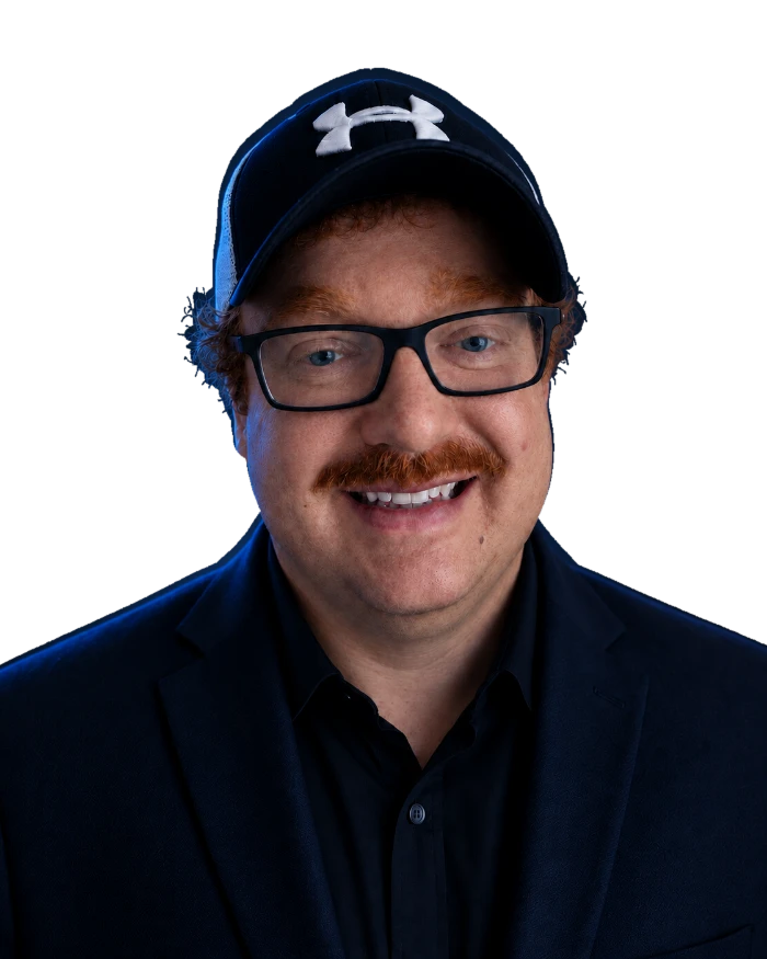 Matt, smiling, in a navy baseball cap and dark-rimmed glasses, with red hair and a mustache, wearing a navy jacket over a dark shirt.
